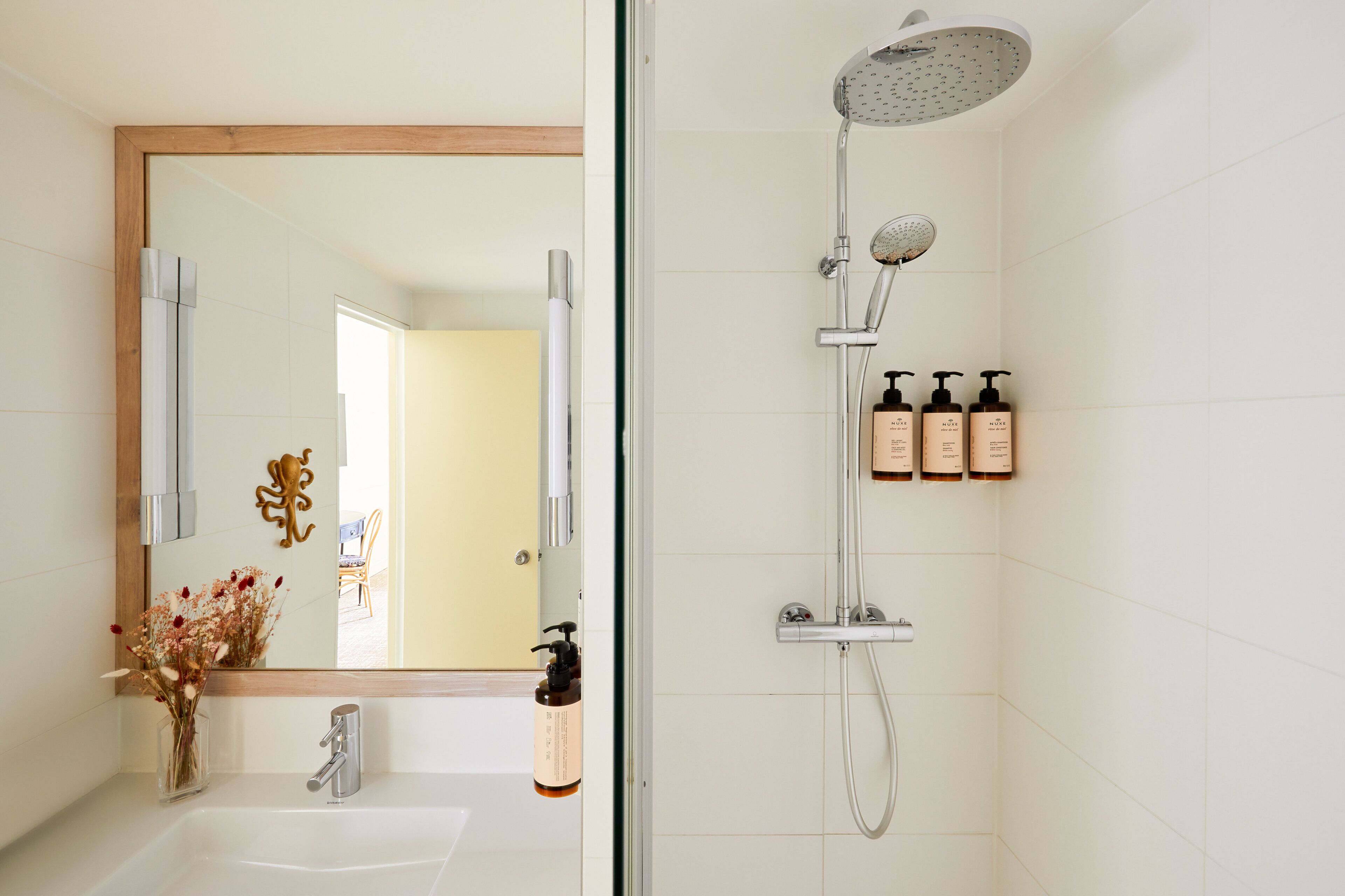 A modern bathroom with a glass shower enclosure, a large mirror, and a sink with toiletries.