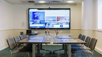 A conference room with a large screen, a table with chairs, and bottles of Abatilles wine.