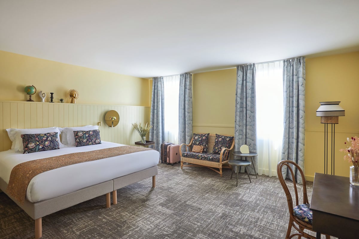 Ein Hotelzimmer mit einem großen Bett, einer Couch, einem Esstisch und Vorhängen.