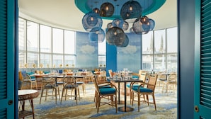 A spacious dining area with round tables and wicker chairs, large windows offering city views, and a ceiling with hanging spherical light fixtures. - Hotel Indigo Bordeaux Centre Chartrons by IHG (Bordeaux)