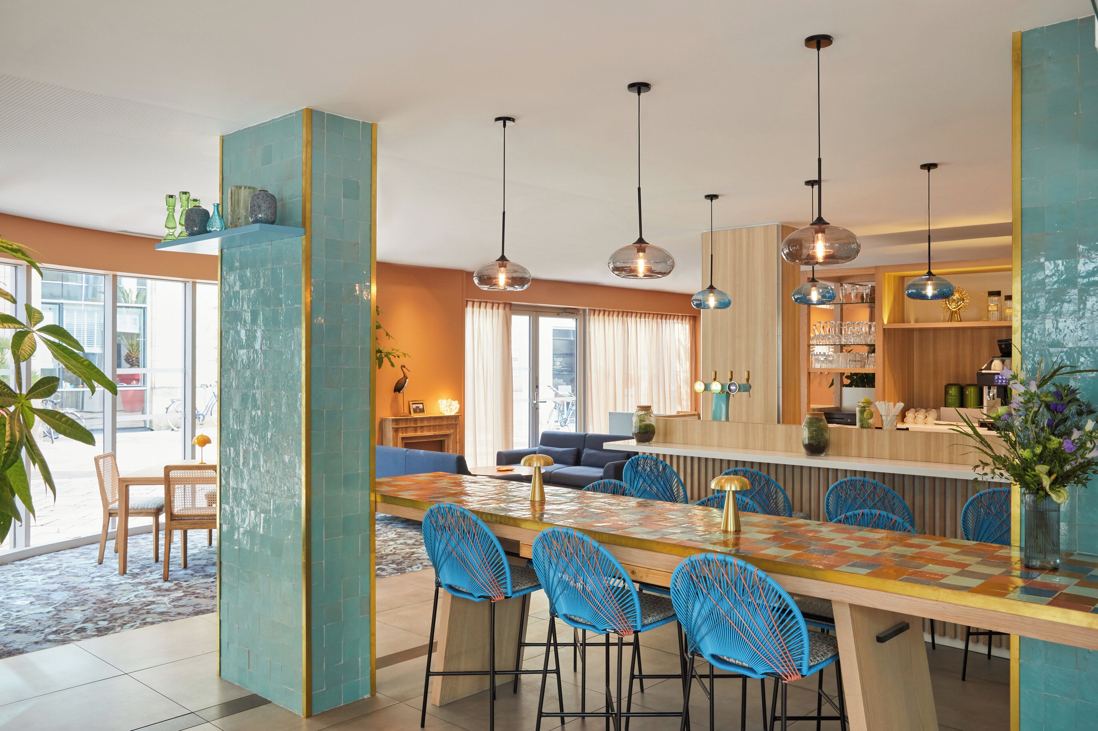 A modern kitchen with a central island, pendant lighting, and a dining area with blue chairs.