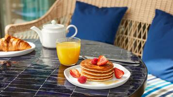 Desayuno con panqueques, fresas y jugo de naranja sobre una mesa.