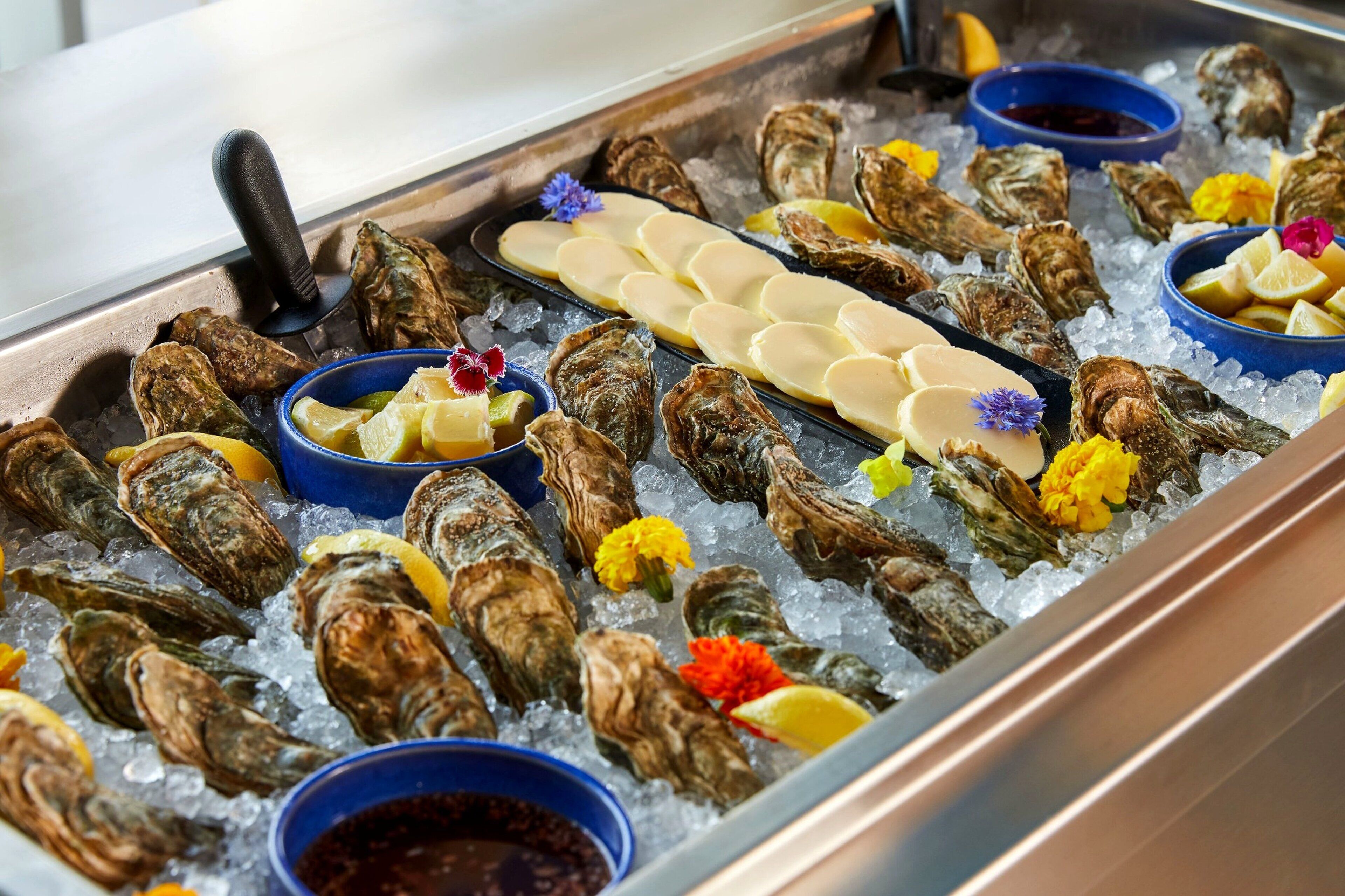 Exhibición de mariscos con ostras sobre hielo, adornadas con rodajas de limón y flores.