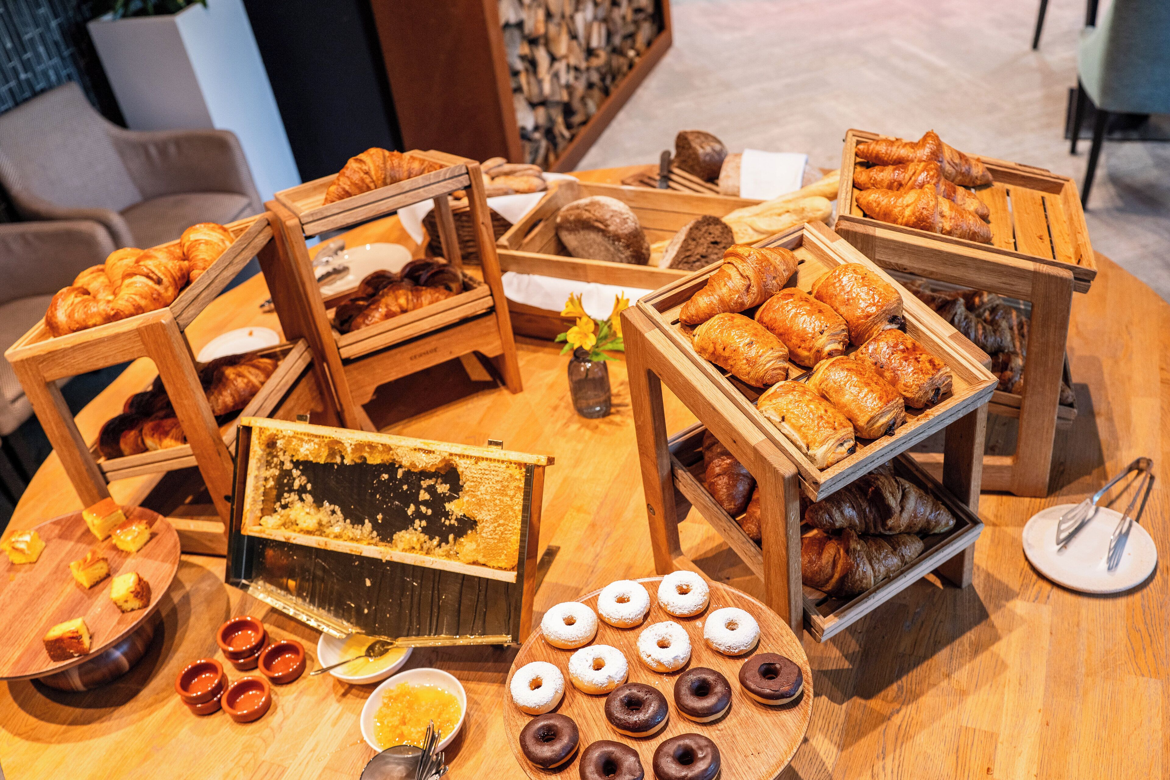 A variety of baked goods displayed on wooden stands, including croissants, pastries, and donuts.