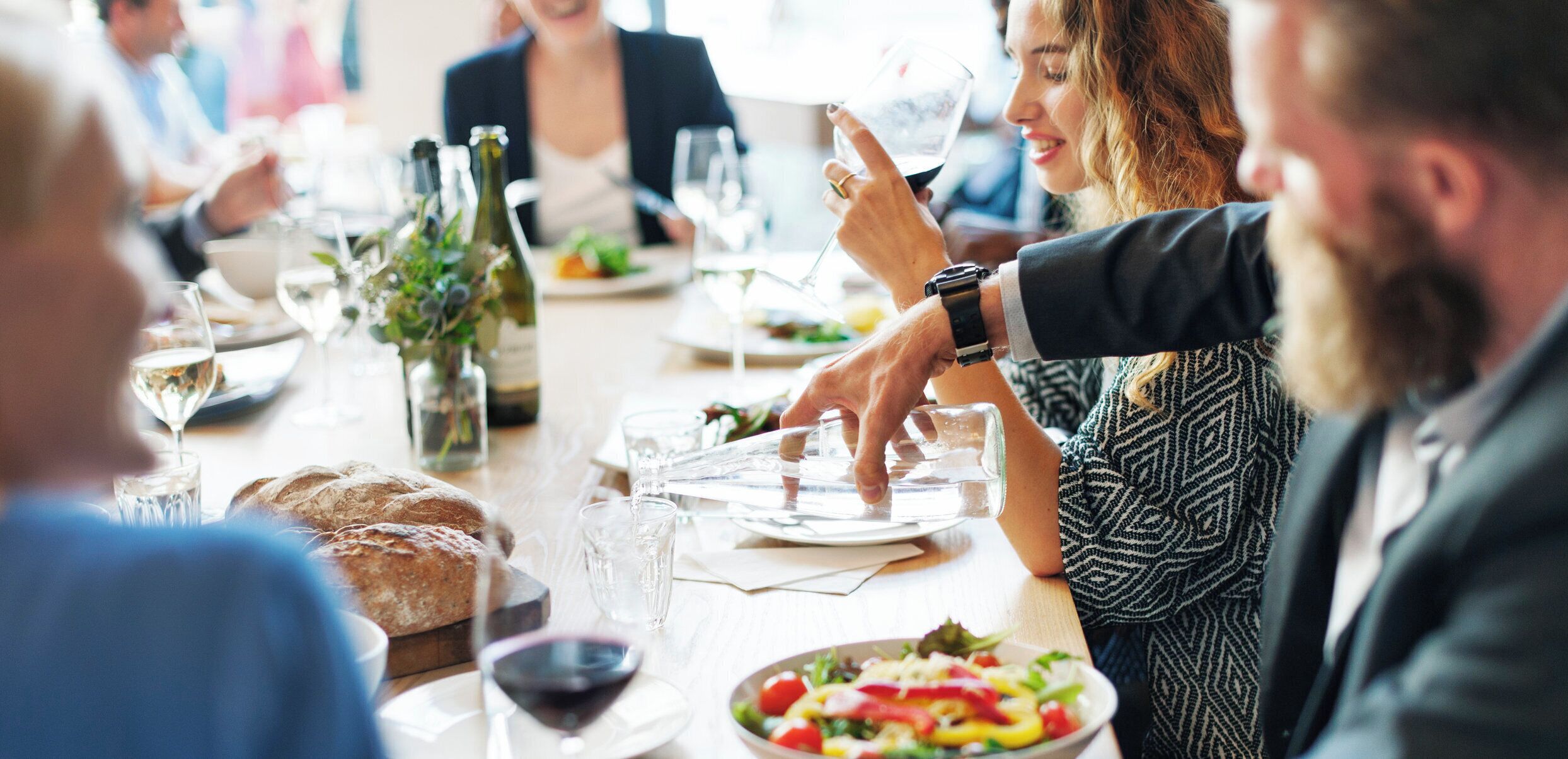 Un grupo de personas cenando en una mesa con diferentes platos, vasos y botellas.