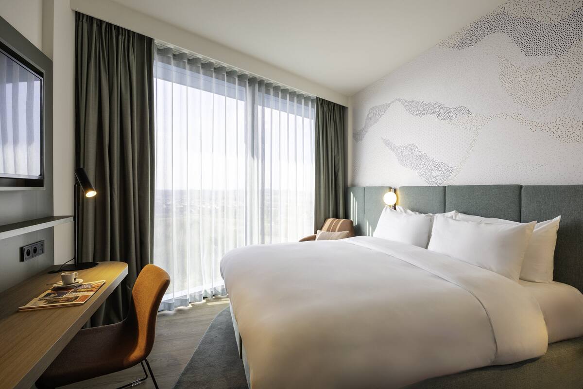 Ein Hotelzimmer mit einem großen Bett, einem Schreibtisch mit Stuhl, einem Fernseher und einer Weltkarte an der Wand.