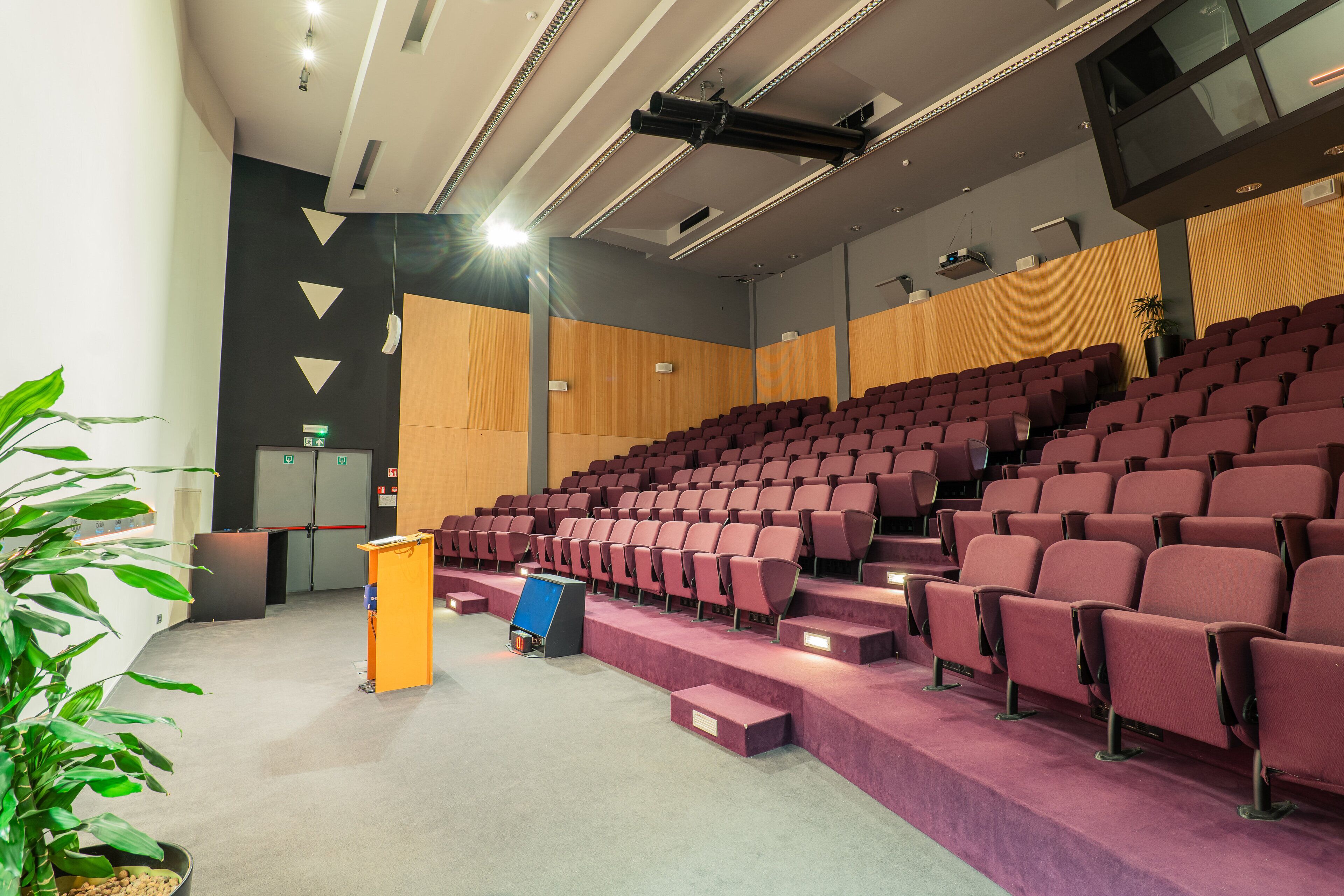 A modern auditorium with tiered seating, a podium, and a large screen.