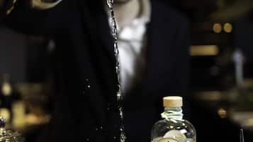A bartender pouring a drink into a glass with a lemon slice, surrounded by various bottles and garnishes.