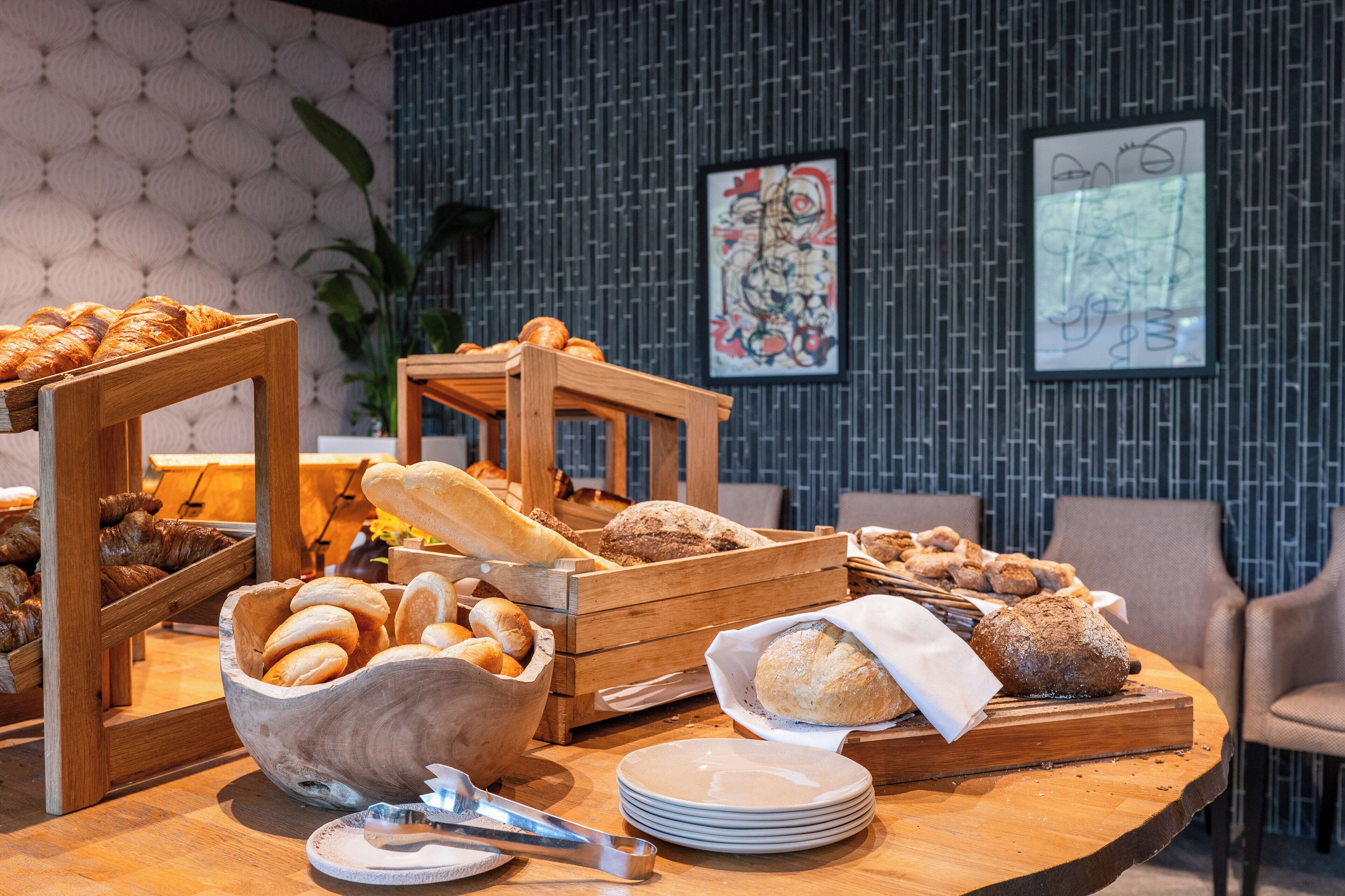 A breakfast buffet with various breads and pastries displayed in wooden crates and bowls.