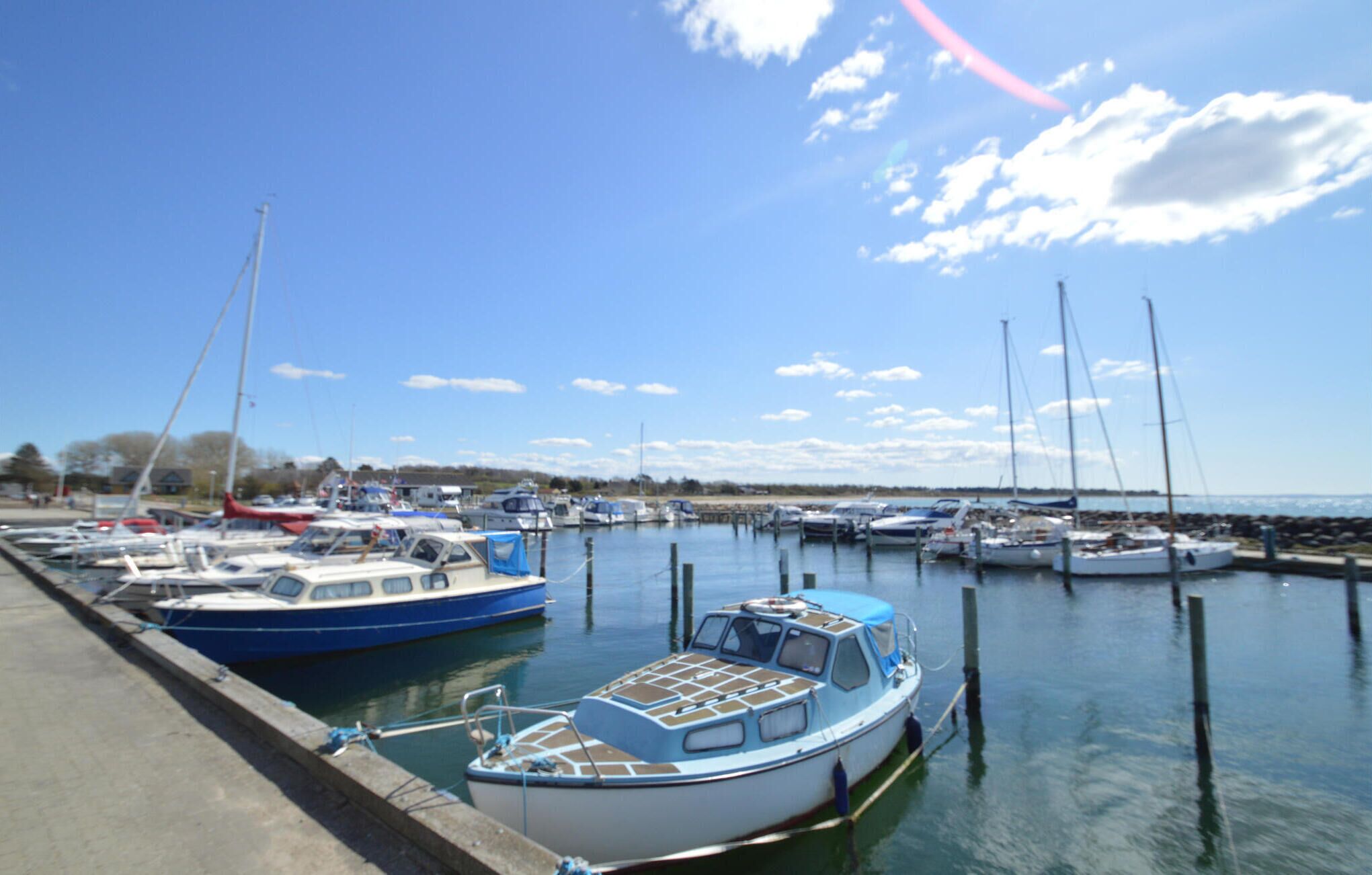 Un port de plaisance où plusieurs bateaux sont amarrés, un ciel dégagé et une eau calme.