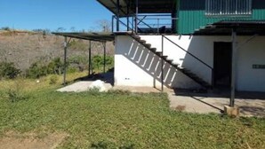 Ein Gebäude mit grüner Fassade, einer Treppe, die zu einem überdachten Bereich führt, und einem Feldweg davor.