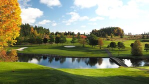 En golfbana med en damm, träd med höstfärgade löv och en klar himmel.