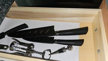 Un cajón con varias herramientas, como un destornillador de sacacorchos, un cuchillo y un alicate.