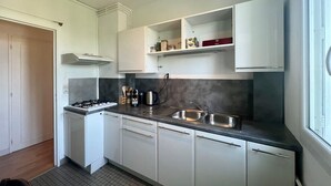 Una cocina moderna con armarios blancos, estufa a gas, un lavamanos y un ventanal que proporciona luz natural.