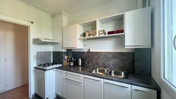 Une cuisine moderne avec des meubles blancs, une cuisinière à gaz, un évier et une fenêtre qui laisse entrer la lumière naturelle.