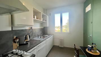Une cuisine de taille réduite, équipée d’une cuisinière à gaz, d’un évier et d’une fenêtre laissant entrer la lumière naturelle.