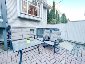 Enjoy al fresco dining on the patio with a metal table and chairs, surrounded by lush greenery and a charming view.