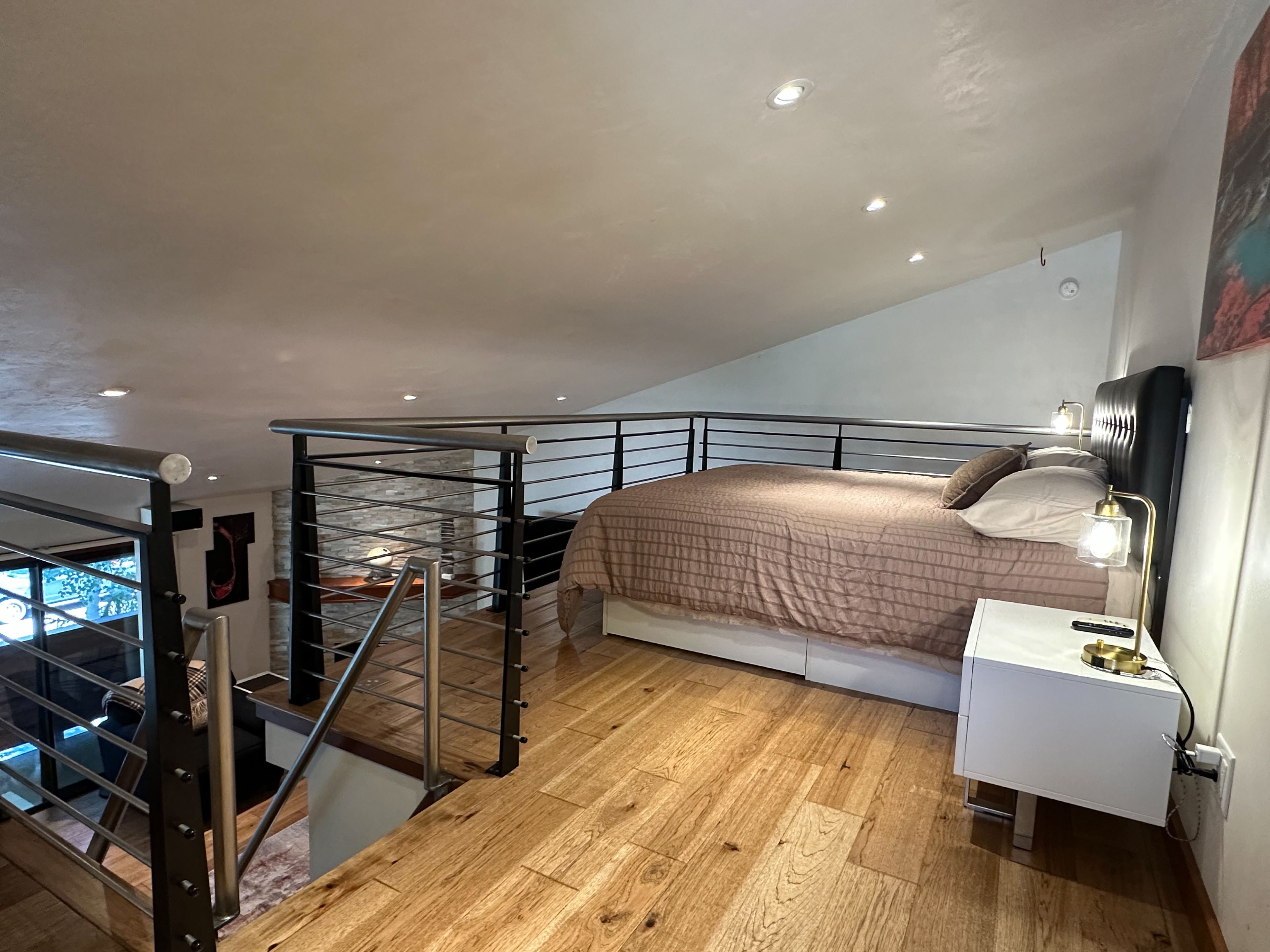 Un dormitorio con cama, mesita de noche, lámpara y una escalera que conduce a un nivel superior.