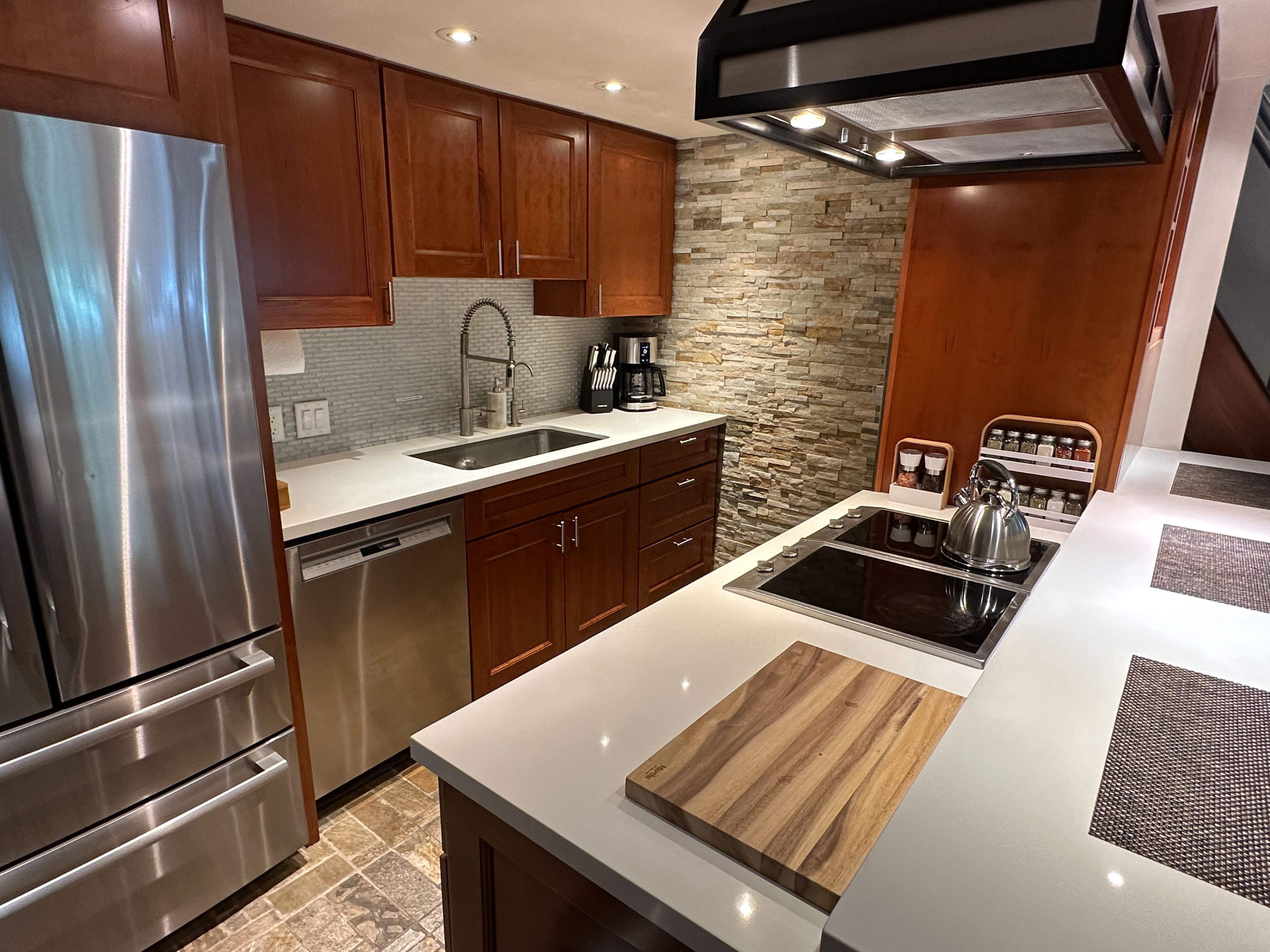Una cocina moderna con electrodomésticos de acero inoxidable, armarios de madera, un protector contra salpicaduras de piedra y una estufa empotrada.