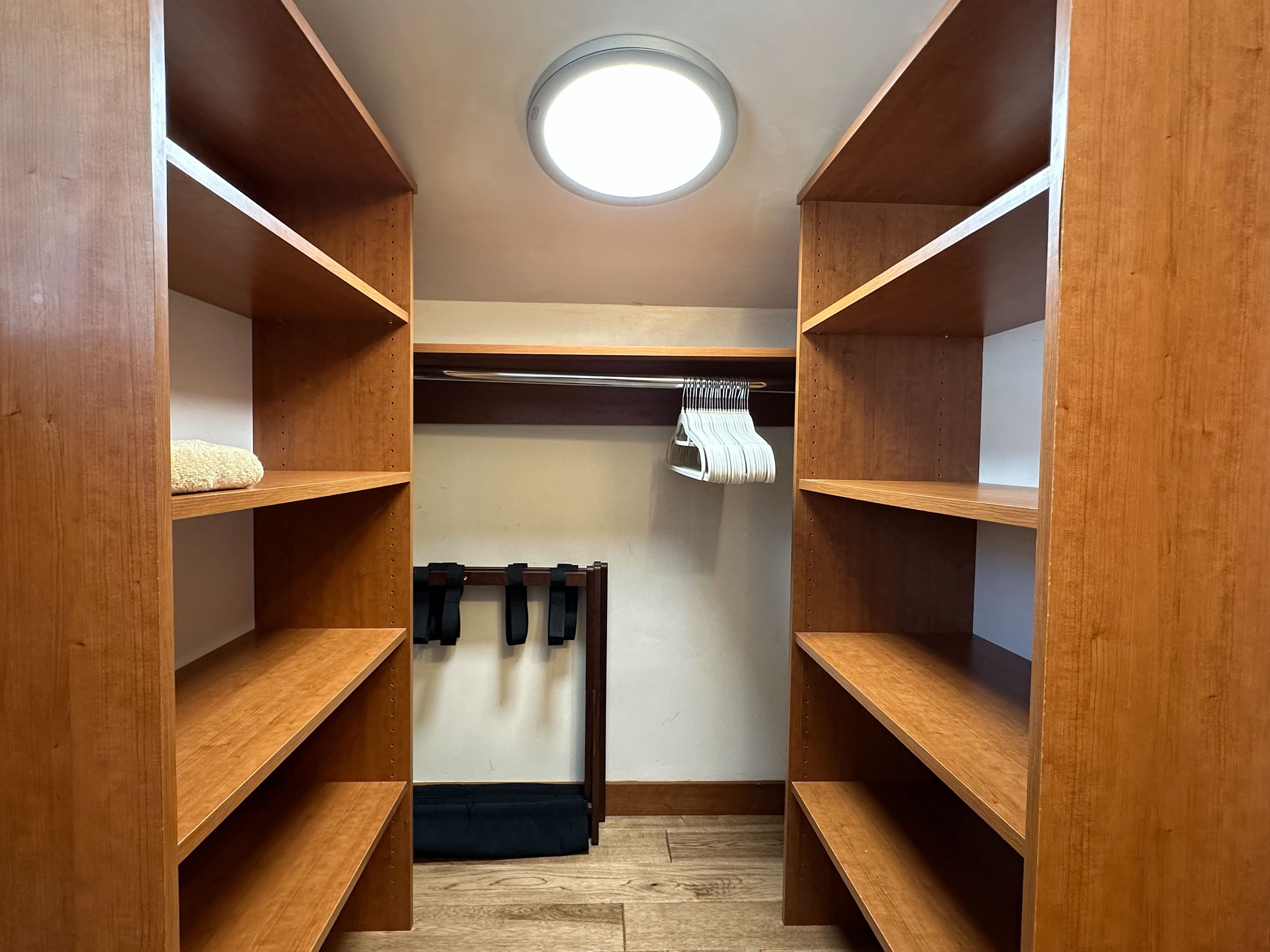Un armario espacioso con estantes de madera, barra para colgar ropa y una lámpara de techo circular.