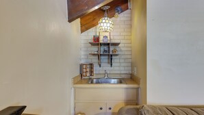Een compacte keuken met een houten plafond, een hangende lamp, een spoelbak en een klein schap met keukenbenodigdheden.