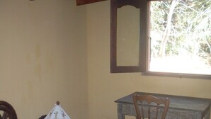 A bedroom with a bed, a wooden desk, a chair, and a window with a view of trees.