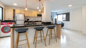 A modern kitchen with wooden cabinets, a central island with stools, a built-in washing machine, and pendant lighting. - Stylish 2BR unit in the Best Scene in Medellin next to Poblado Park (Medellín)