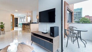 A modern living room with a flat-screen TV mounted on the wall, a wooden entertainment unit, and a dining area with a table and chairs. - Stylish 2BR unit in the Best Scene in Medellin next to Poblado Park (Medellín)