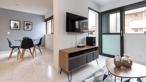A modern living room with a dining area, a flat-screen TV mounted on the wall, and a large window offering a view of the outside. - Stylish 2BR unit in the Best Scene in Medellin next to Poblado Park (Medellín)