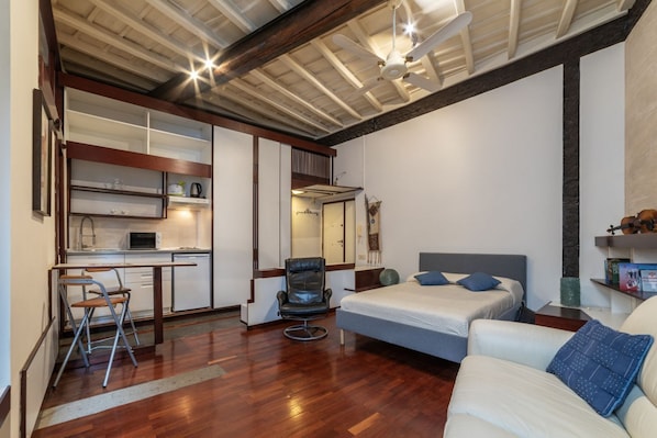 A compact room with a bed, a desk, a chair, and a kitchenette.