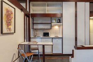 A compact kitchen with a microwave, kettle, and sink. There is a small dining area with a table and chairs.