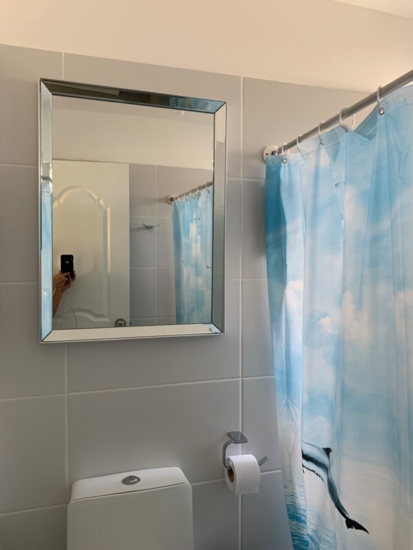 A bathroom with a shower curtain featuring a whale design, a toilet, and a mirror on the wall. - Piscis Playa (Tumbes)