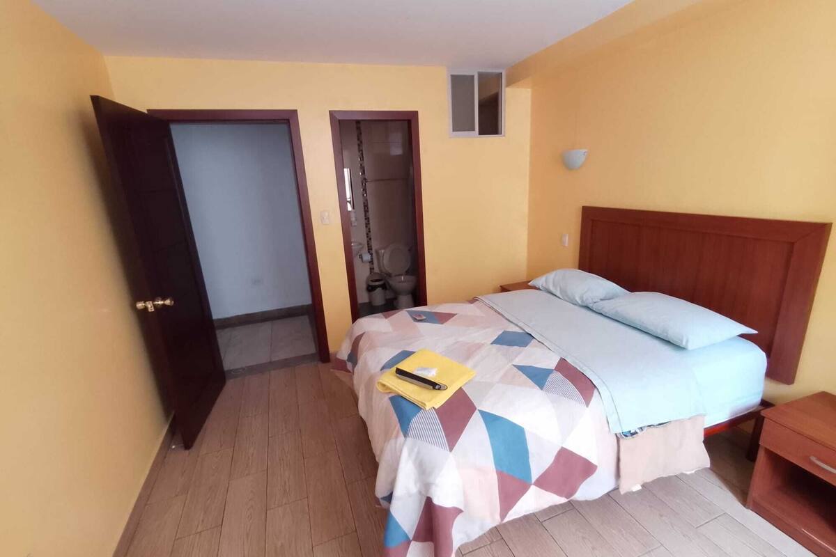 A bedroom with a bed, a wooden headboard, a bedside table, and a small window.