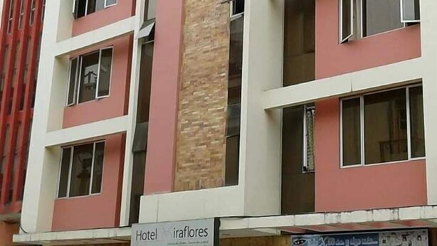 A hotel building with multiple floors, each with a balcony. The facade is a combination of red and beige colors. There are signs indicating the hotel name. - Hotel Residencial Miraflores (Loja)