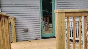 Eine Holzterrasse führt zu einem Haus mit grüner Tür, einer kleinen Veranda und einem Geländer.