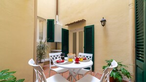 A small outdoor dining area with a round table, white chairs, and a potted plant.