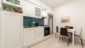 A modern kitchen with white cabinetry, a teal backsplash, and a dining area with a table and chairs.