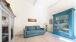 A room with a light-colored wooden floor, a teal sofa, a blue cabinet with decorative items, and a framed picture on the wall.