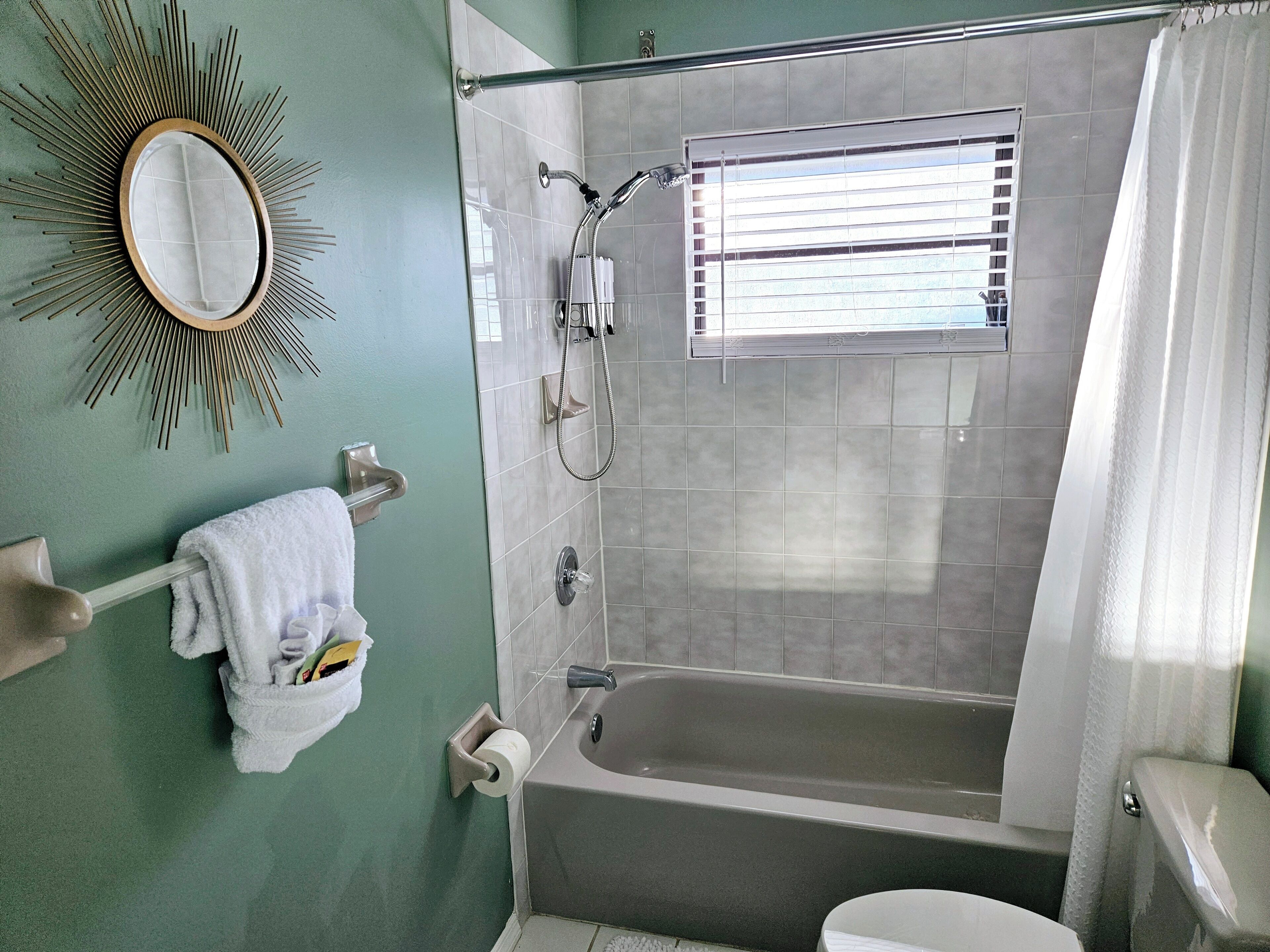 A bathroom with a bathtub, a shower, a toilet, a towel rack with towels, and a mirror.