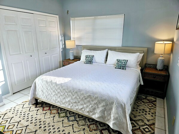 A neatly made bed with white bedding, two bedside lamps, a patterned rug, and a closed door. - Escape the Ordinary and Experience Island Paradise (Big Pine Key)