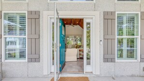 A modern house entrance with a glass door, a beige sofa inside, and a view of greenery outside. - Oleander Cottage! Pet Friendly, Heated Pool, Private Escape, 2 Minutes to Beaches and Restaurants (Saint Simons Island)
