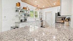A modern kitchen with white cabinetry, granite countertops, and a wooden ceiling. - Oleander Cottage! Pet Friendly, Heated Pool, Private Escape, 2 Minutes to Beaches and Restaurants (Saint Simons Island)