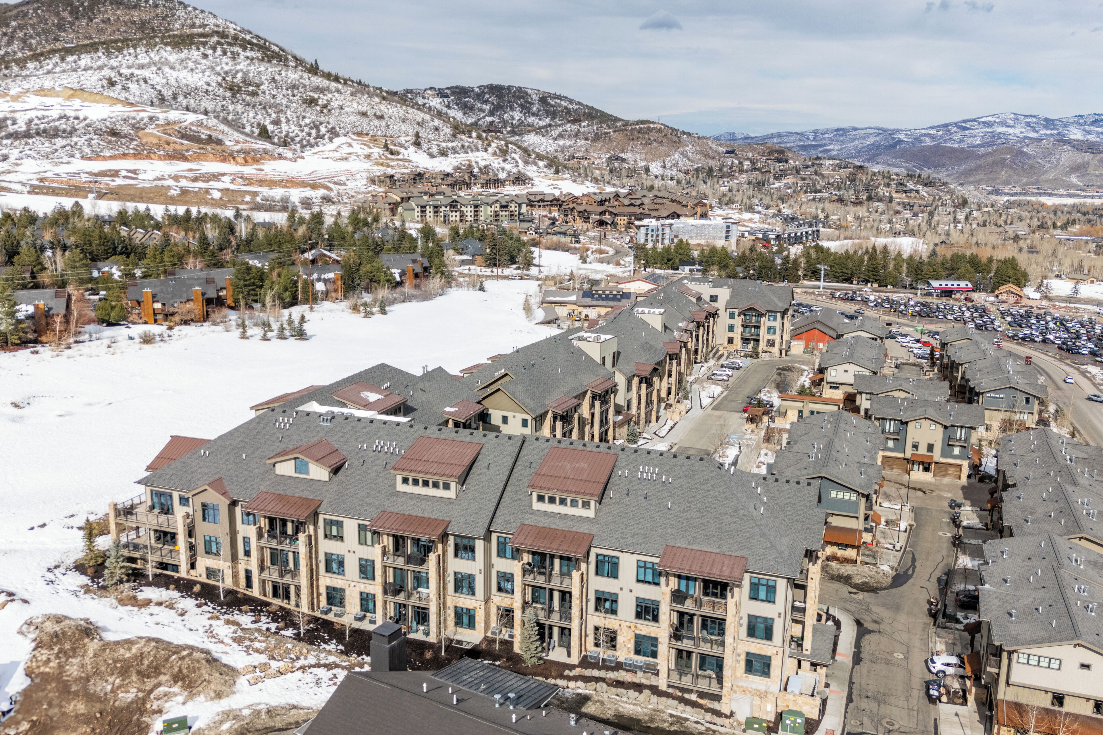 Un hôtel à plusieurs étages offrant une vue sur une station de ski, doté d’un parking et surplombant un paysage montagneux.