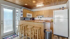 Cocina con armarios de madera, un refrigerador blanco, un microondas y una zona con taburetes de bar.