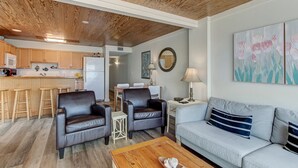 Una cocina moderna con armarios de madera, un comedor con mesa y sillas, una sala de estar con sofá y mesa de centro, y un cuadro en la pared.
