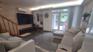 Ein modernes Wohnzimmer mit Flachbildfernseher, einer Treppe und einer Glastür, die auf einen Balkon führt.