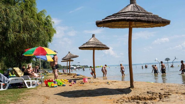 Ein Strand mit Reetdachschirmen, Liegestühlen und badenden Personen.