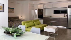 En moderne stue med en grøn sofa, et spisebord med en plante, og et køkken med mikroovn og ovn.