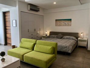 Une chambre à coucher moderne avec un lit, deux tables de chevet, une armoire et un canapé vert.