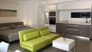 En moderne stue med en grøn sofa, et hvidt sofabord og en seng med mønstret sengetøj.